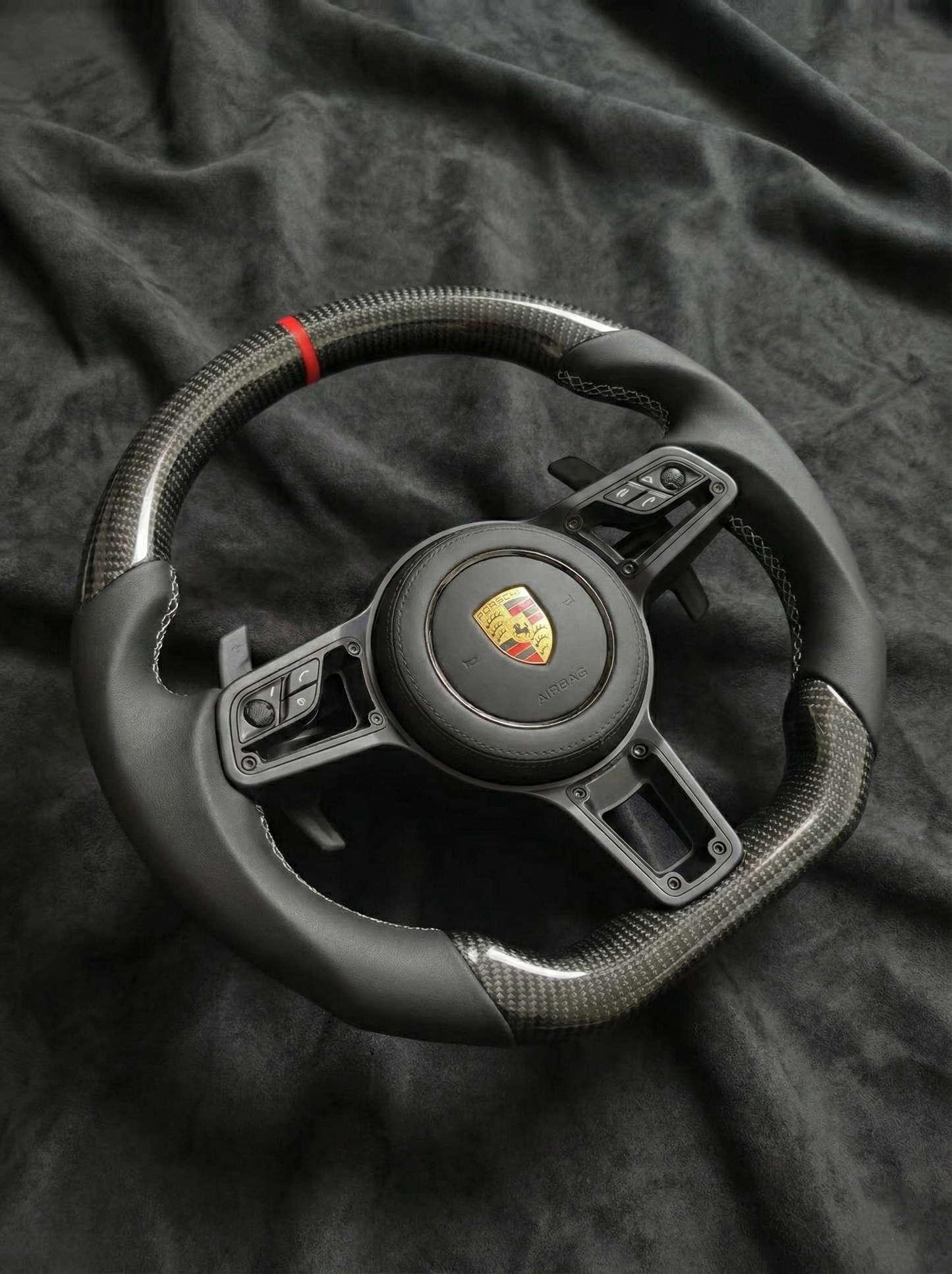 Black steering wheel with Porsche logo on a dark fabric background
