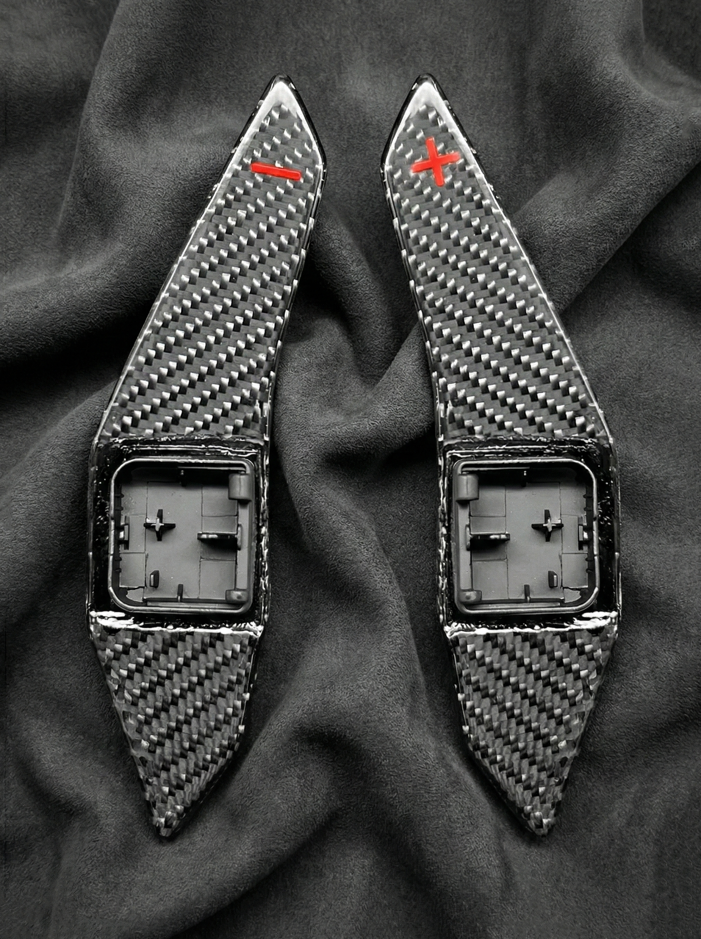 Two carbon fiber patterned objects on a dark fabric background