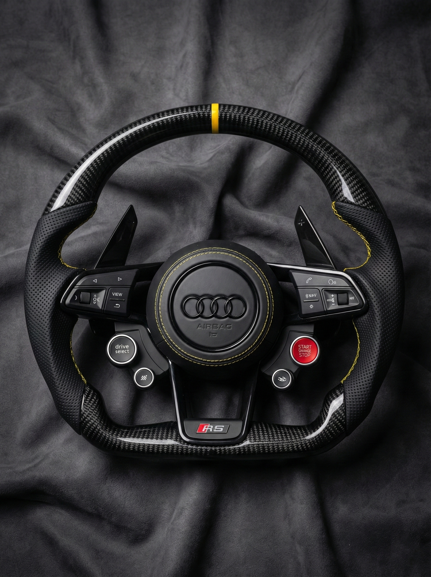 Carbon fiber steering wheel with Audi logo on a dark fabric background