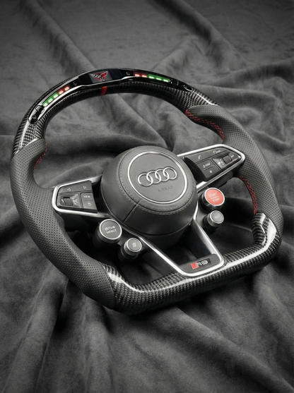 Carbon fiber steering wheel with Audi logo on a dark fabric background