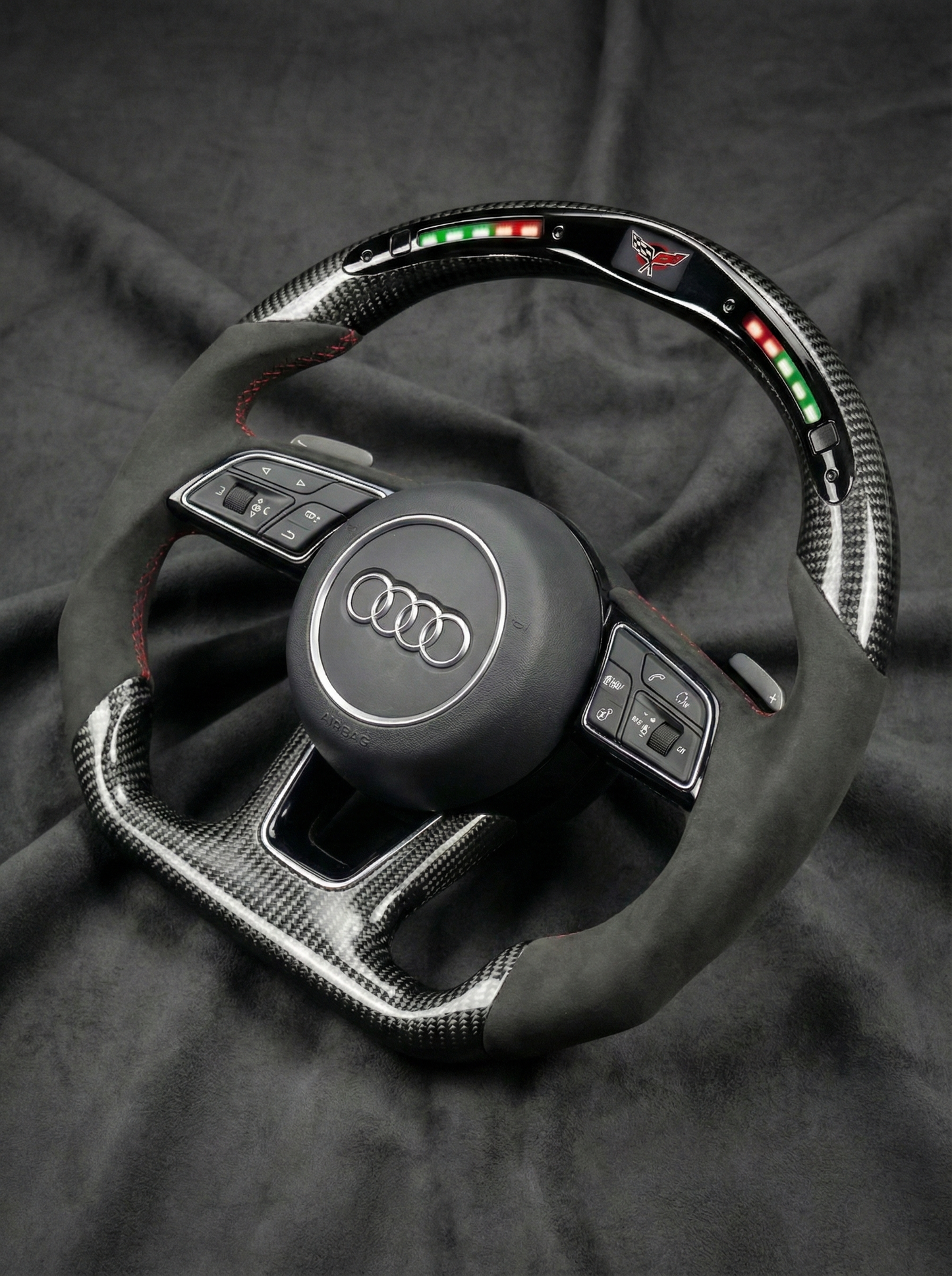 Carbon fiber steering wheel with Audi logo on a dark fabric background