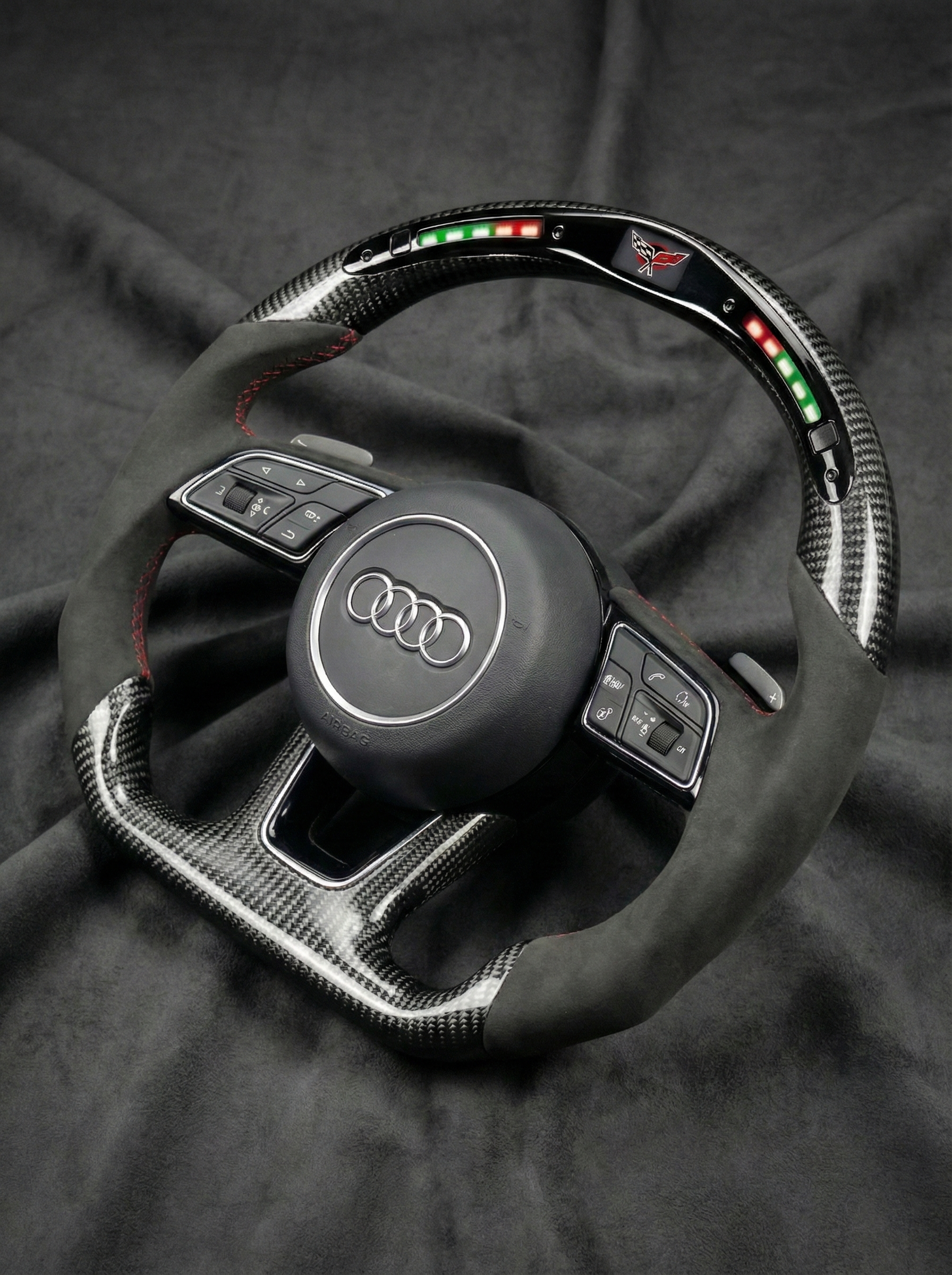 Carbon fiber steering wheel with Audi logo on a dark fabric background