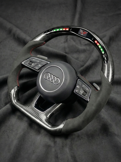 Carbon fiber steering wheel with Audi logo on a dark fabric background