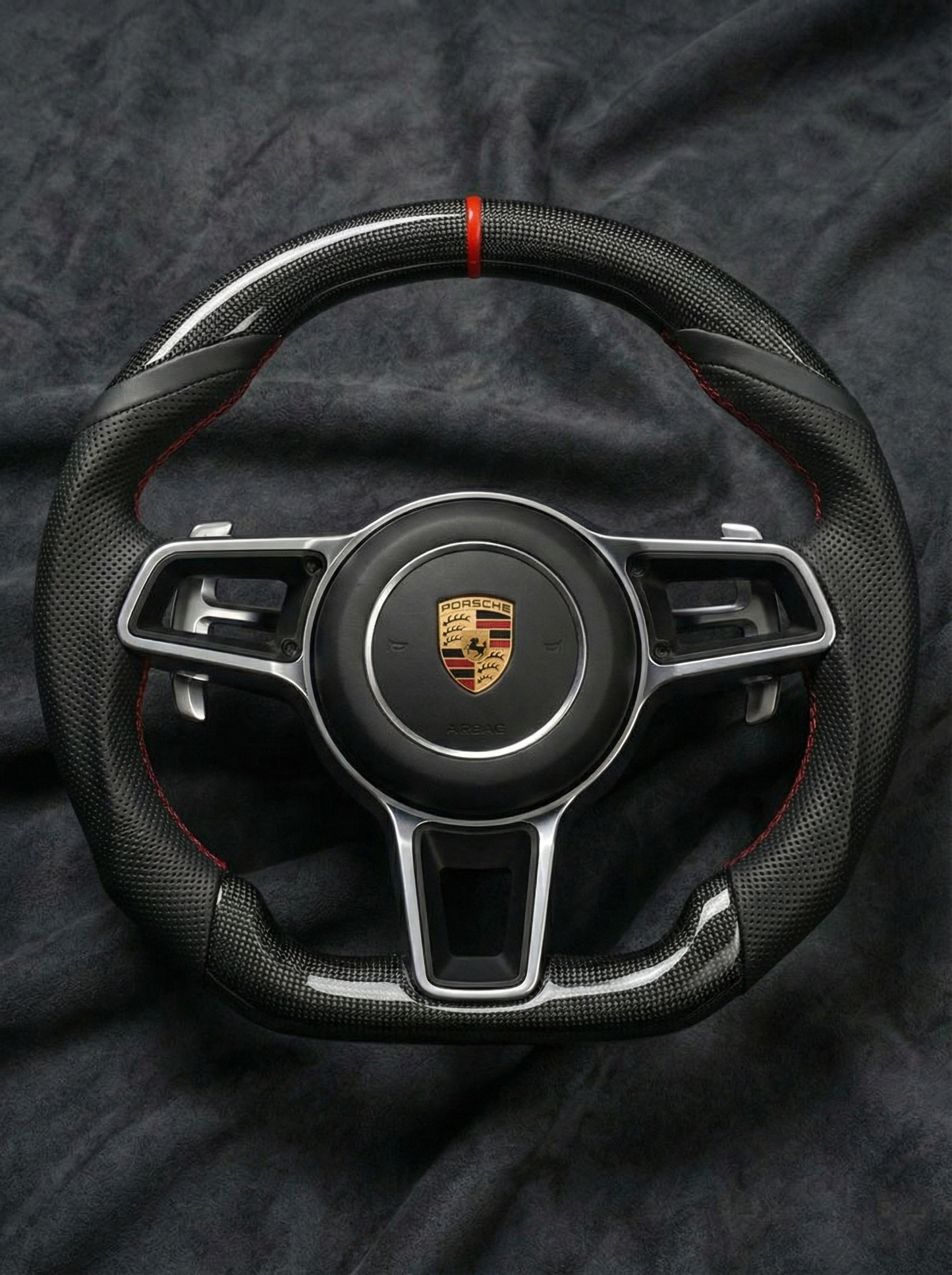 Steering wheel with Porsche logo on a dark fabric background