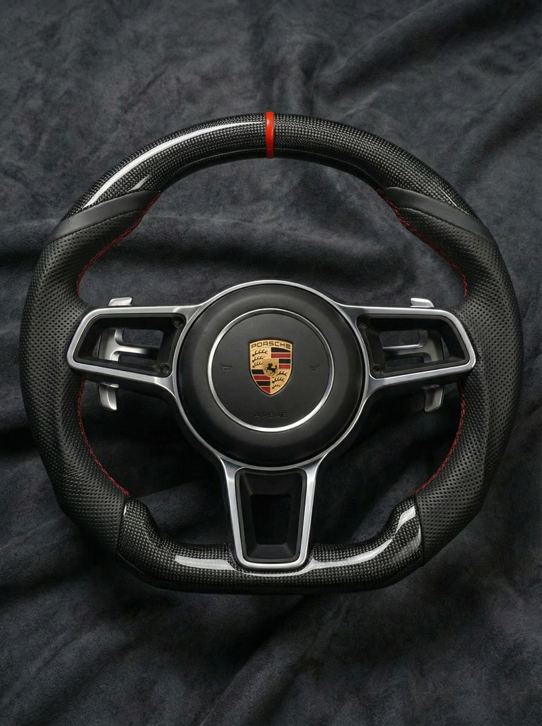Steering wheel with Porsche logo on a dark fabric background