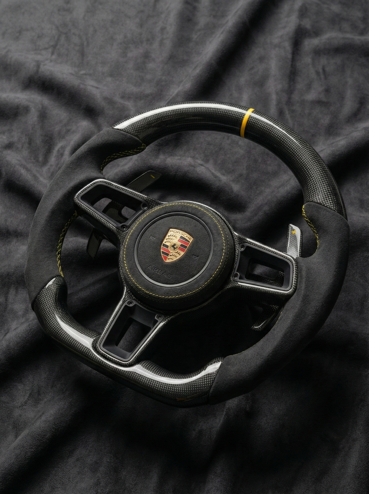 Black steering wheel with Porsche logo on a dark fabric background