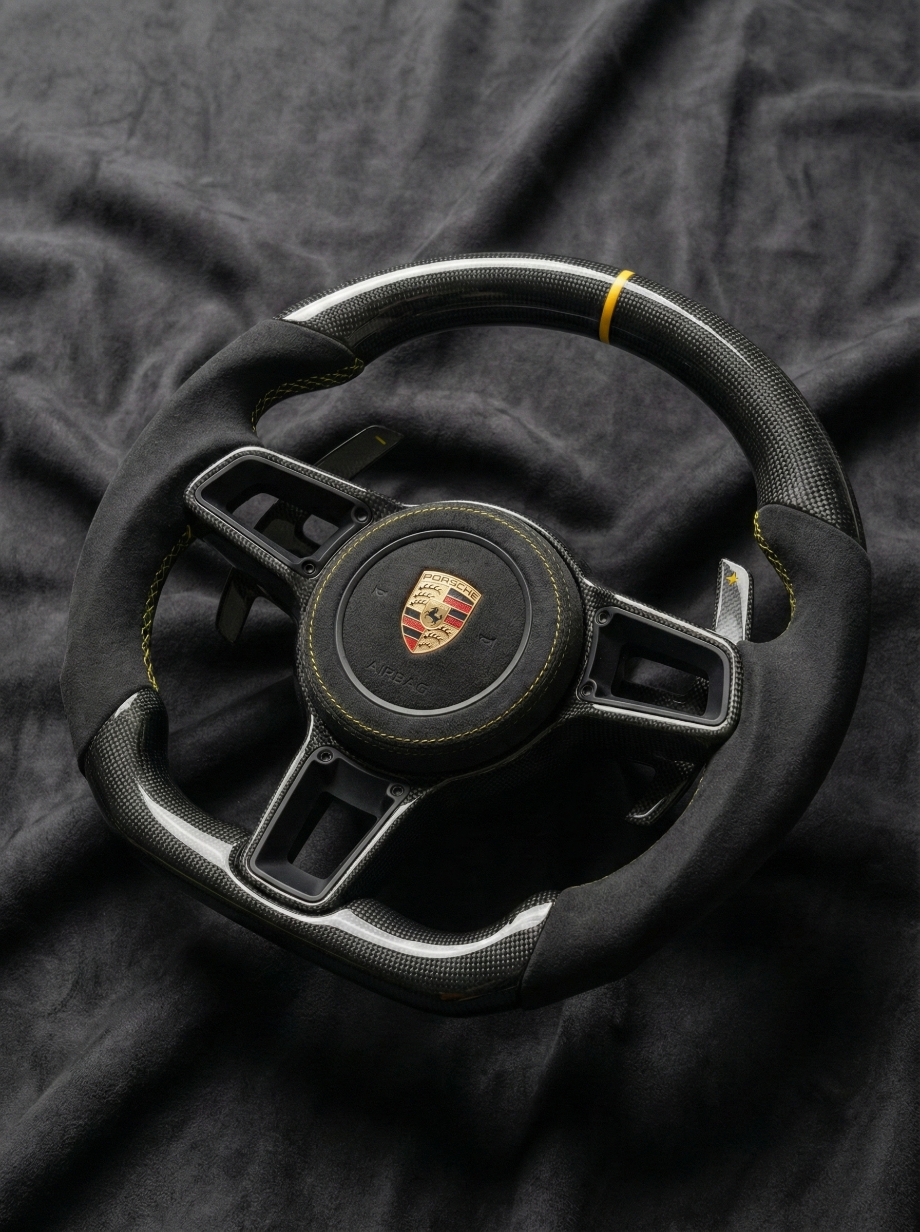 Black steering wheel with Porsche logo on a dark fabric background
