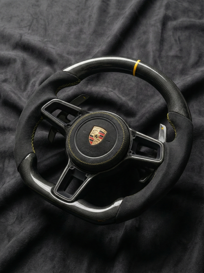 Black steering wheel with Porsche logo on a dark fabric background